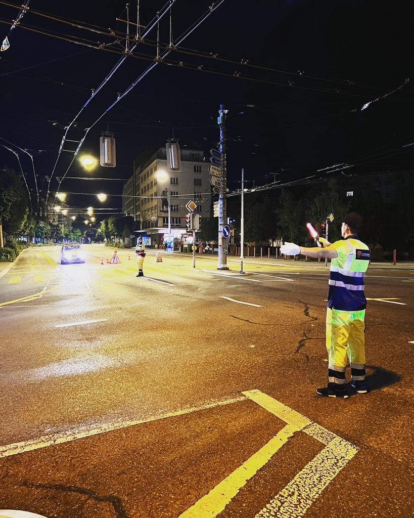 Sicherheitsmitarbeiter regelt den Verkehr nachts an einer großen Kreuzung im Stadtzentrum von Luzern, Pilatusplatz.